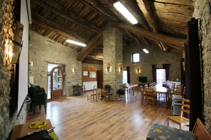 Un interior rústico con paredes de piedra, vigas de madera y un comedor con sillas y mesas.