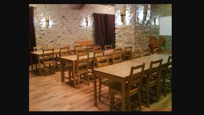 A dining area with wooden tables and chairs, stone walls, and a projector screen. - Albergue Casa Fumenal (Valle de Lierp)