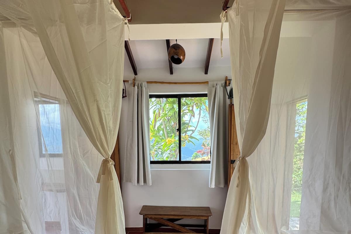 A room with two beds, a bench, and a window with curtains.