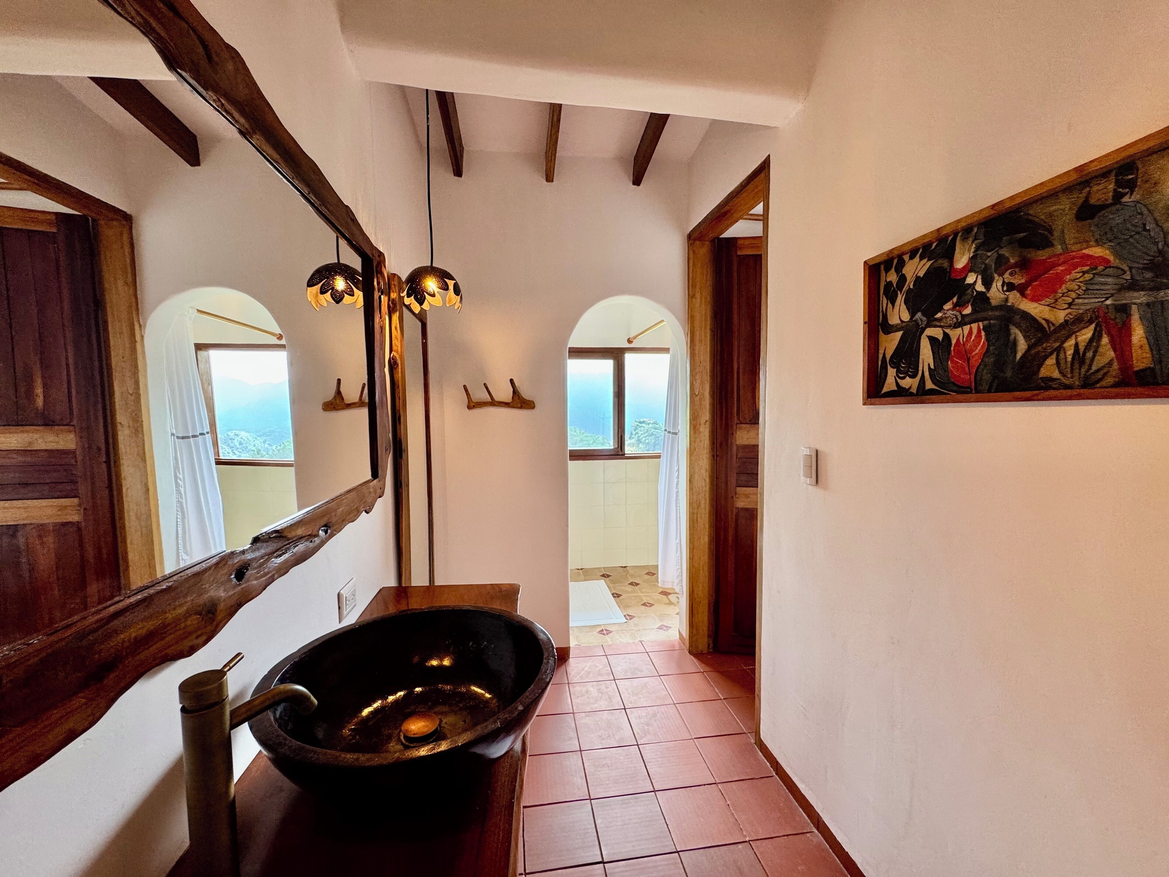 Un pasillo con suelo de madera, un espejo grande, un lavabo negro y un cuadro en la pared.