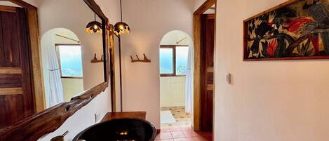 Un pasillo con suelo de madera, un espejo grande, un lavabo negro y un cuadro en la pared.