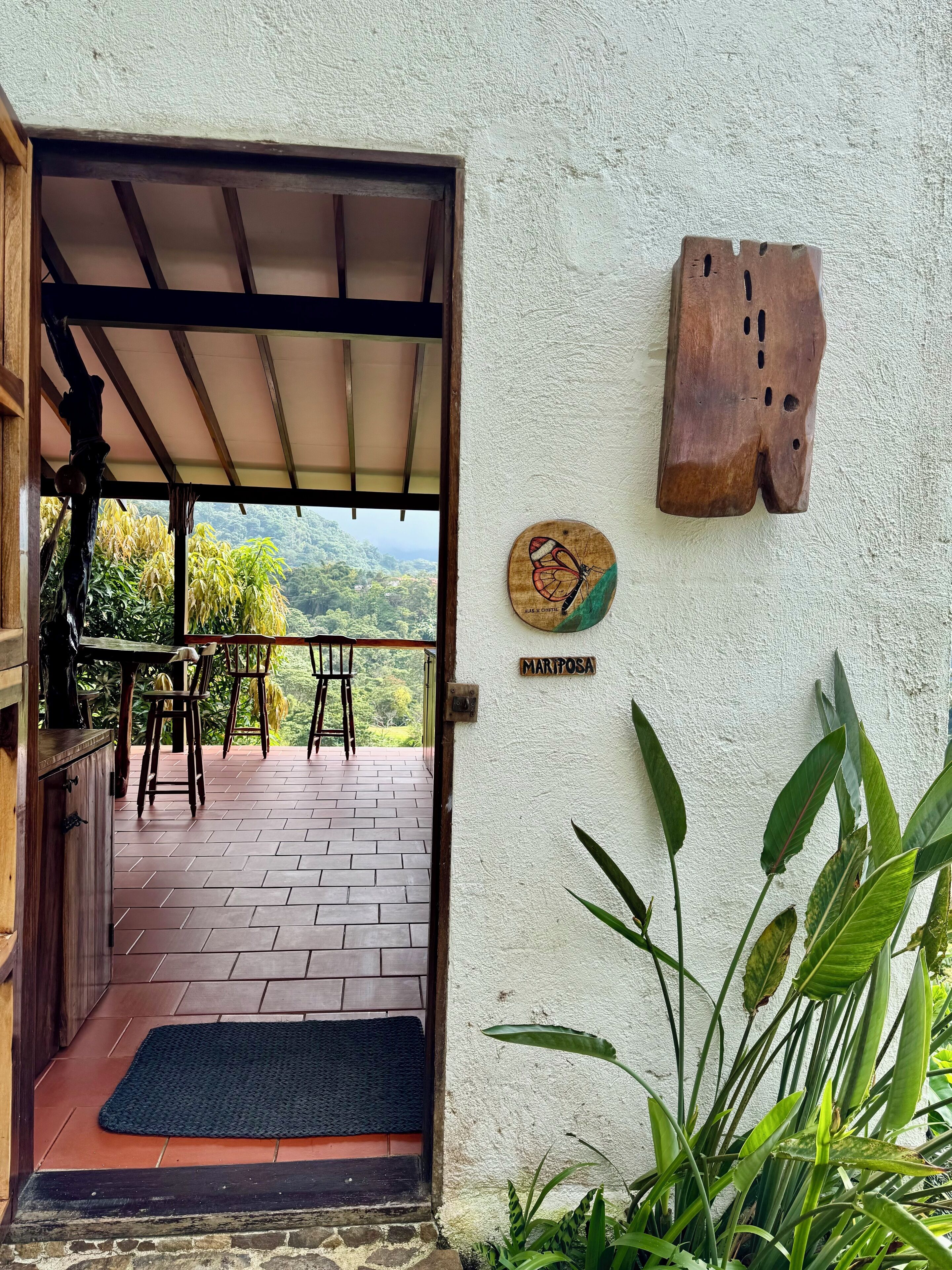 A wooden door leading to a covered patio with a view of lush greenery.