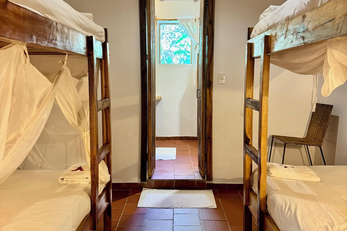A corridor with two wooden bunk beds, a wicker chair, and a view through a doorway.