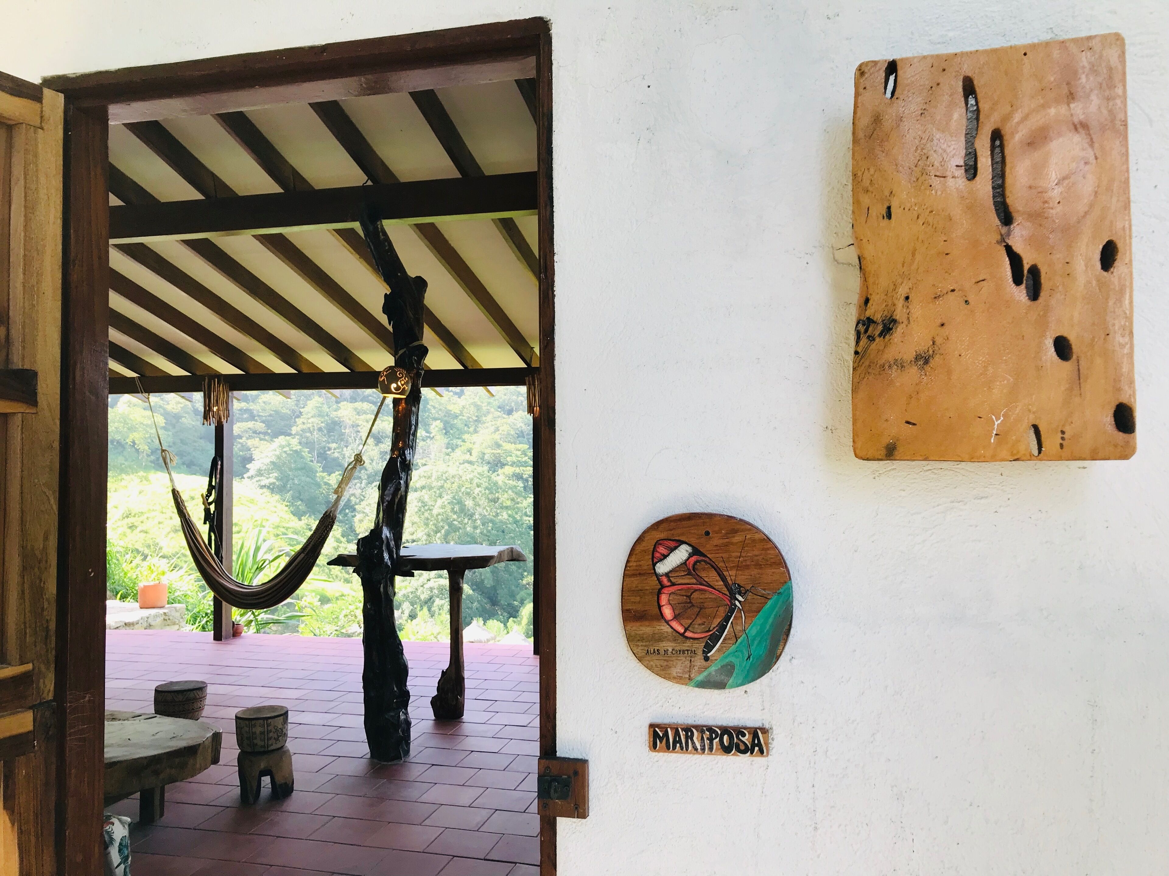 Eine Holztür führt zu einem überdachten Außenbereich mit einer Hängematte, einem Tisch und einem Schild mit der Aufschrift 'MARIPOSA'.