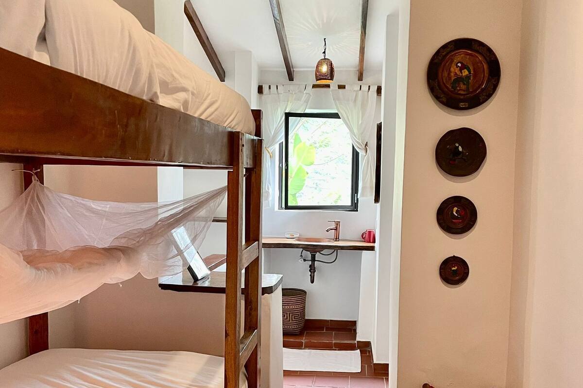 A compact room with bunk beds, a small bathroom, and a window with curtains.