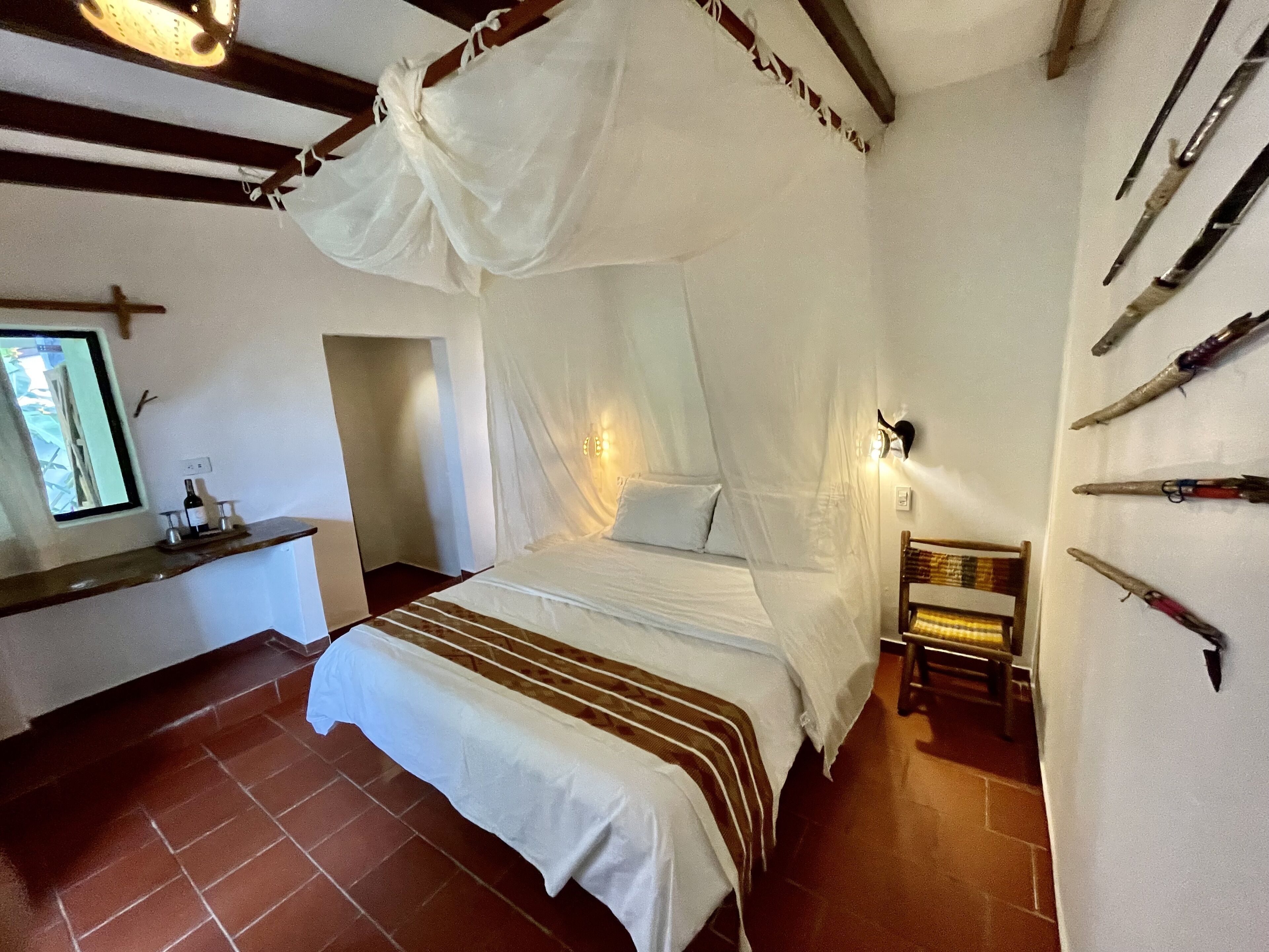 Une chambre avec un lit sous un dais, une petite table avec une bouteille, et un mur orné de différents objets.