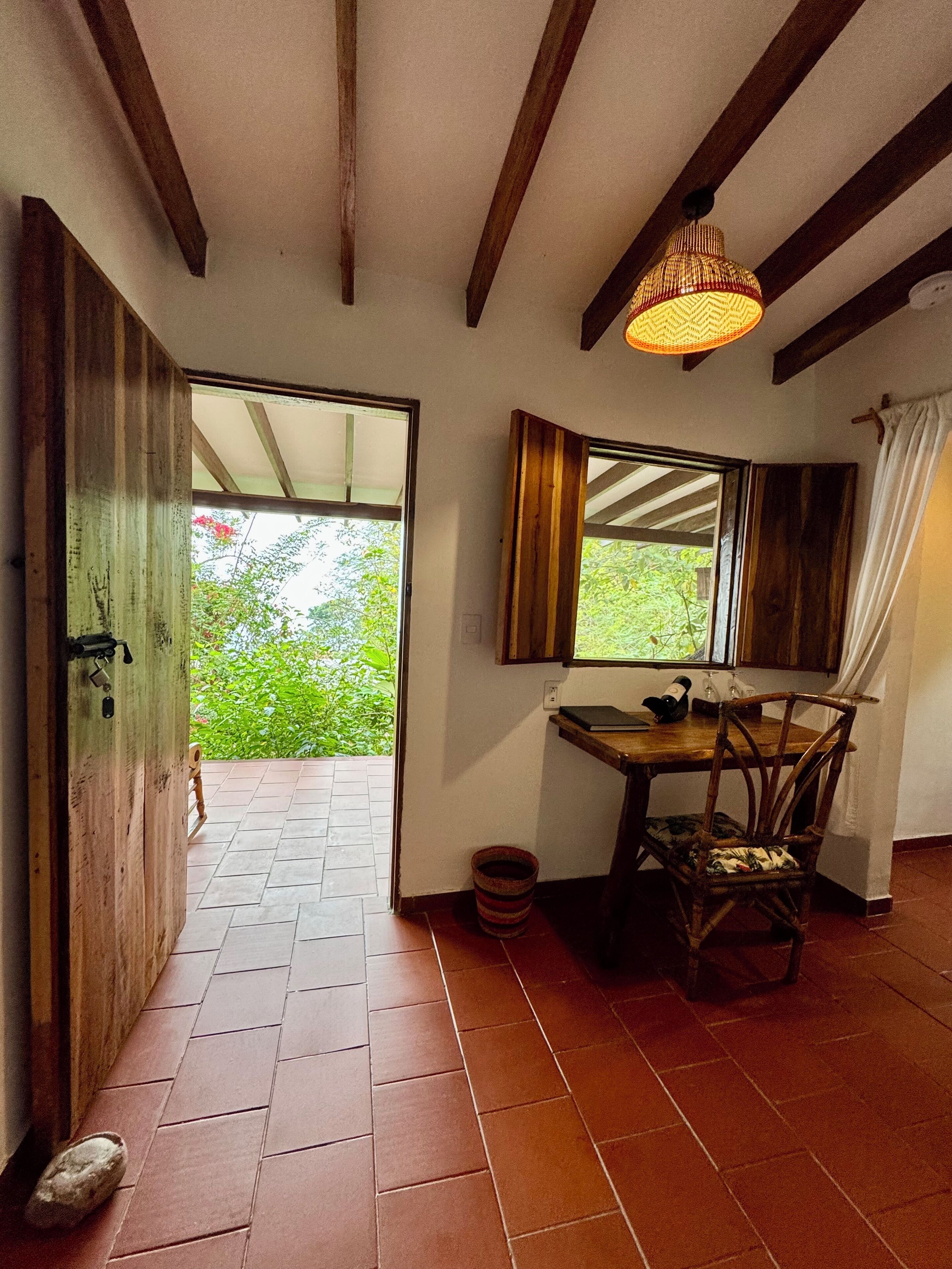A wooden door leading to an outdoor area with a tiled floor and a rustic interior with a wooden table and chair.