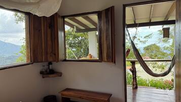 A bedroom with a large window, wooden furniture, and a hammock outside.