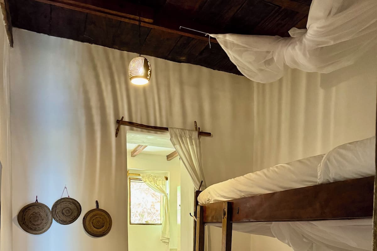 A room with a bunk bed, a small bench, and a door leading to another room.