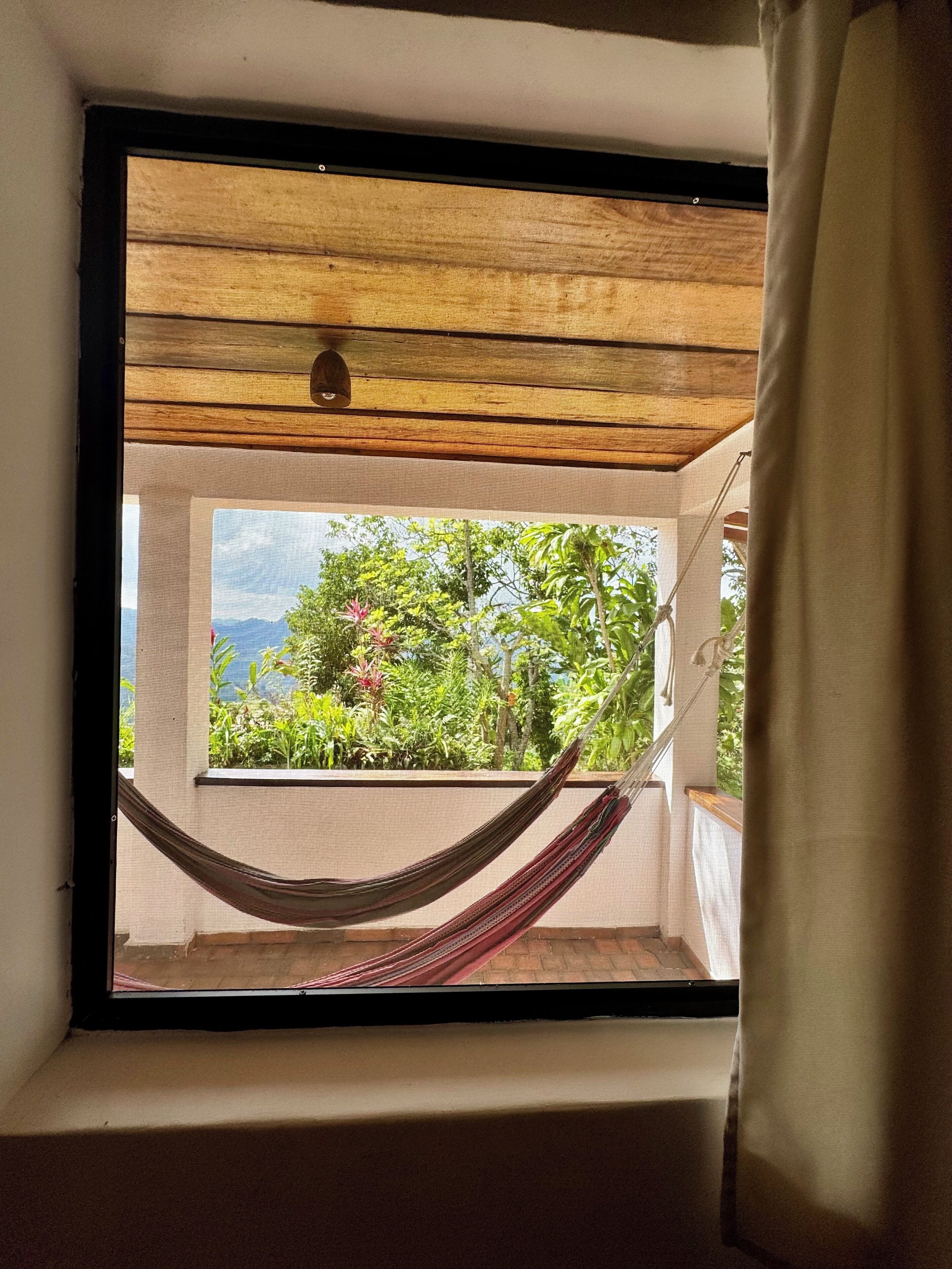 Una hamaca en una ventana con vistas a la vegetación y montañas.