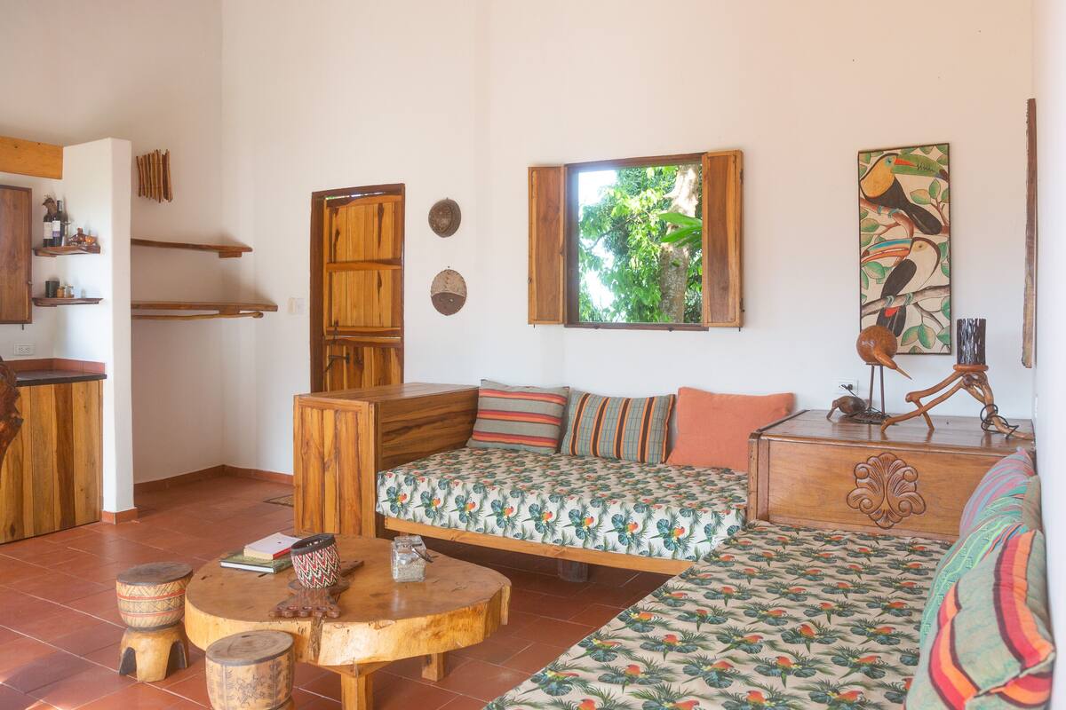 A cozy room with a wooden bed, a small table, and a window with a view of greenery.