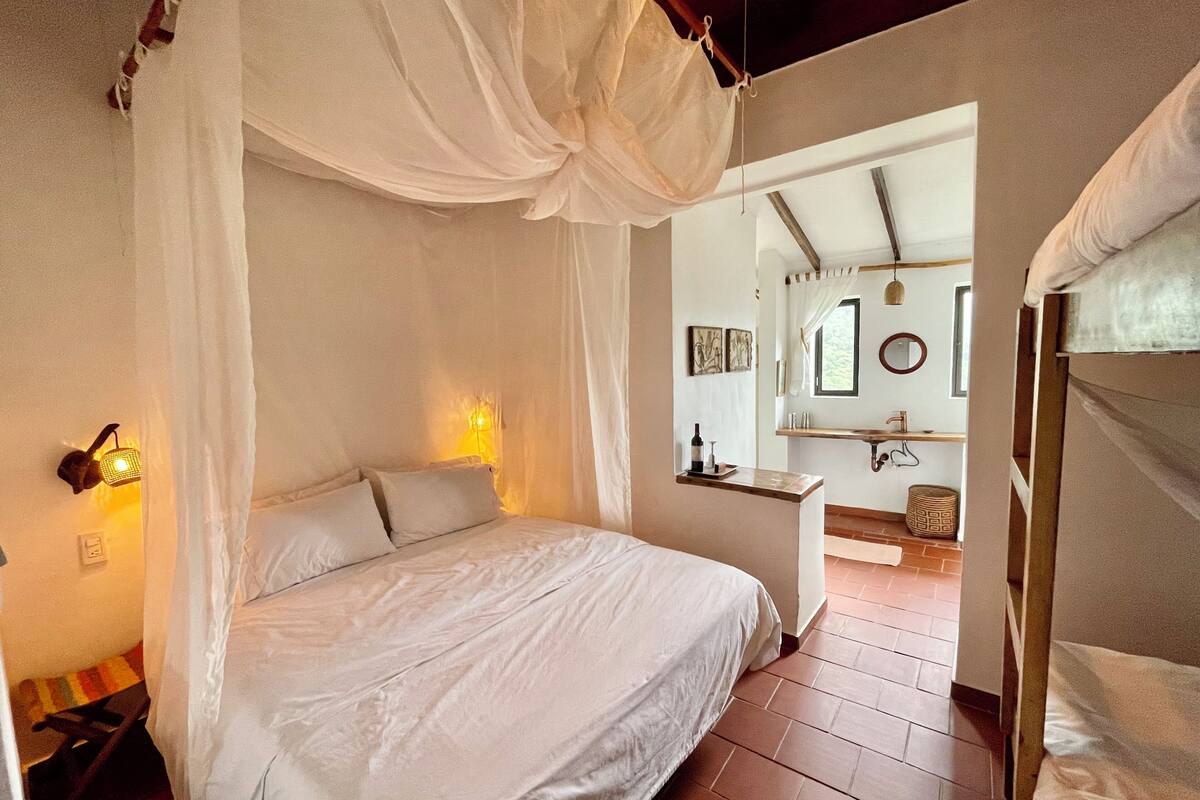 A bedroom with a canopy bed, a bedside table with a bottle, and a mirror above a sink.