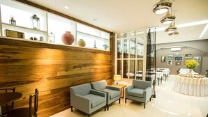 A modern hotel lobby with a wooden accent wall, seating area with sofas and chairs, a dining table, and a buffet setup. - Almasty Hotel (Chapecó)