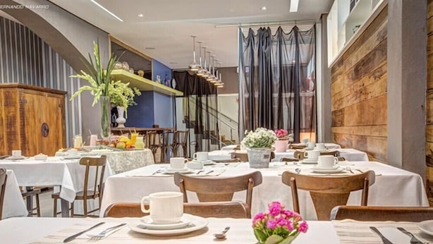 A restaurant with tables set for dining, featuring a mix of wooden and upholstered chairs, and a variety of table settings including plates, cups, and cutlery. - Almasty Hotel (Chapecó)