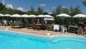 Een buitenzwembad met tafels en parasols, omgeven door groen.