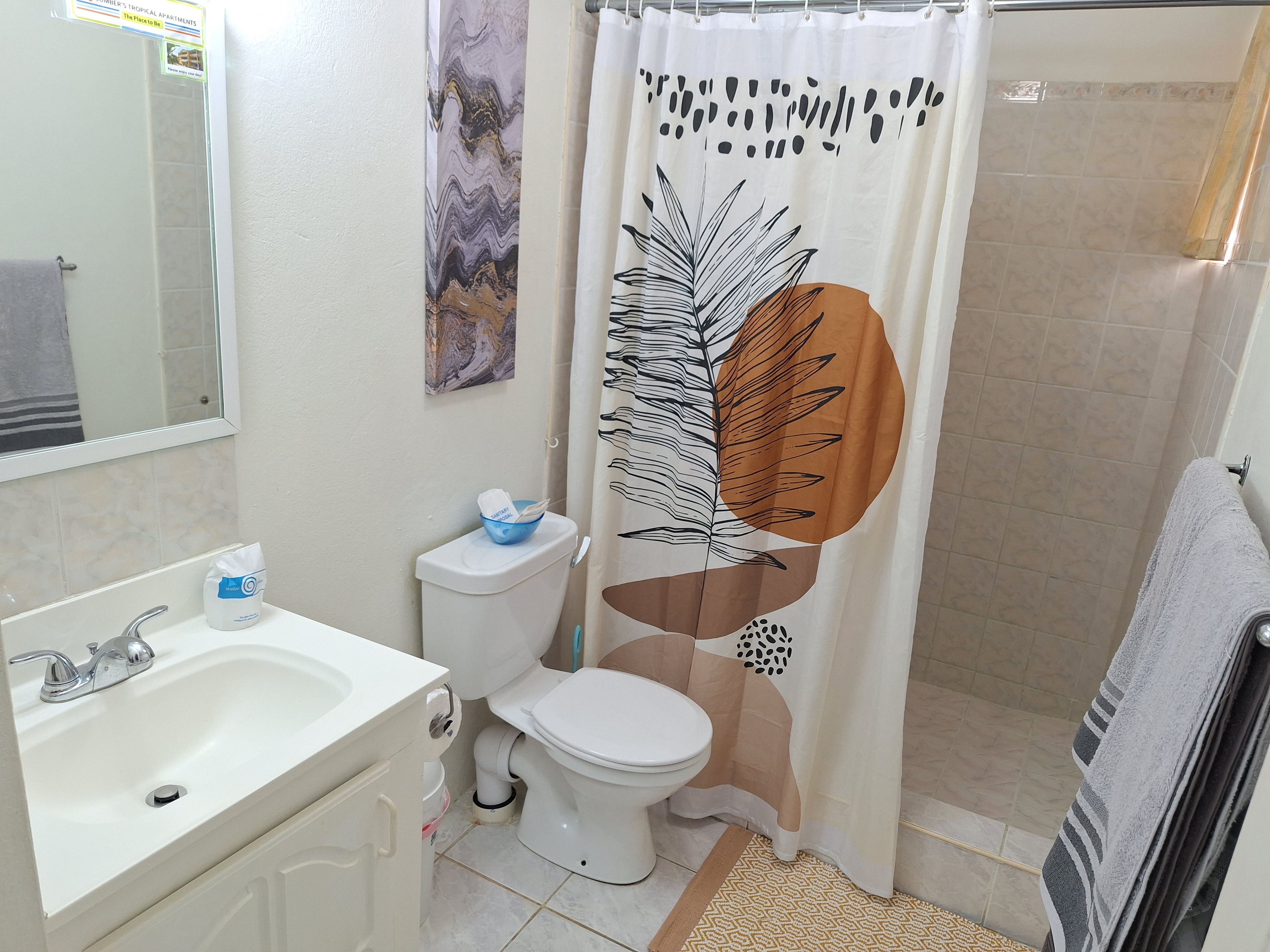 A bathroom with a white sink, a toilet, a shower curtain with a leaf pattern, and a towel rack.