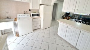 A kitchen with white cabinets, a microwave, a refrigerator, and a washing machine. - Cumber's Tropical Apartments (Oistins)