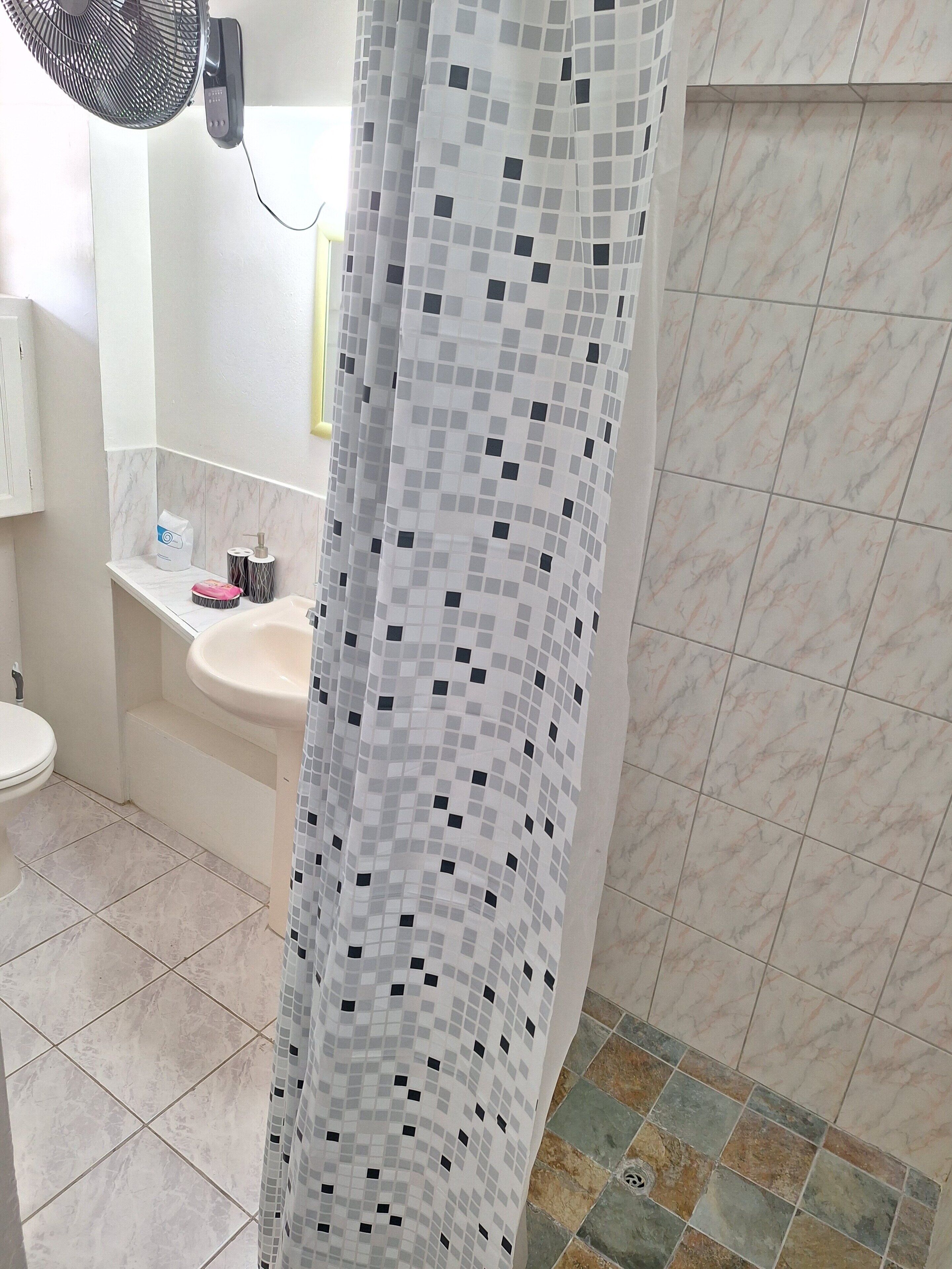 Un bagno con pavimento piastrellato, un lavandino, un water e una tenda da doccia a motivi geometrici.