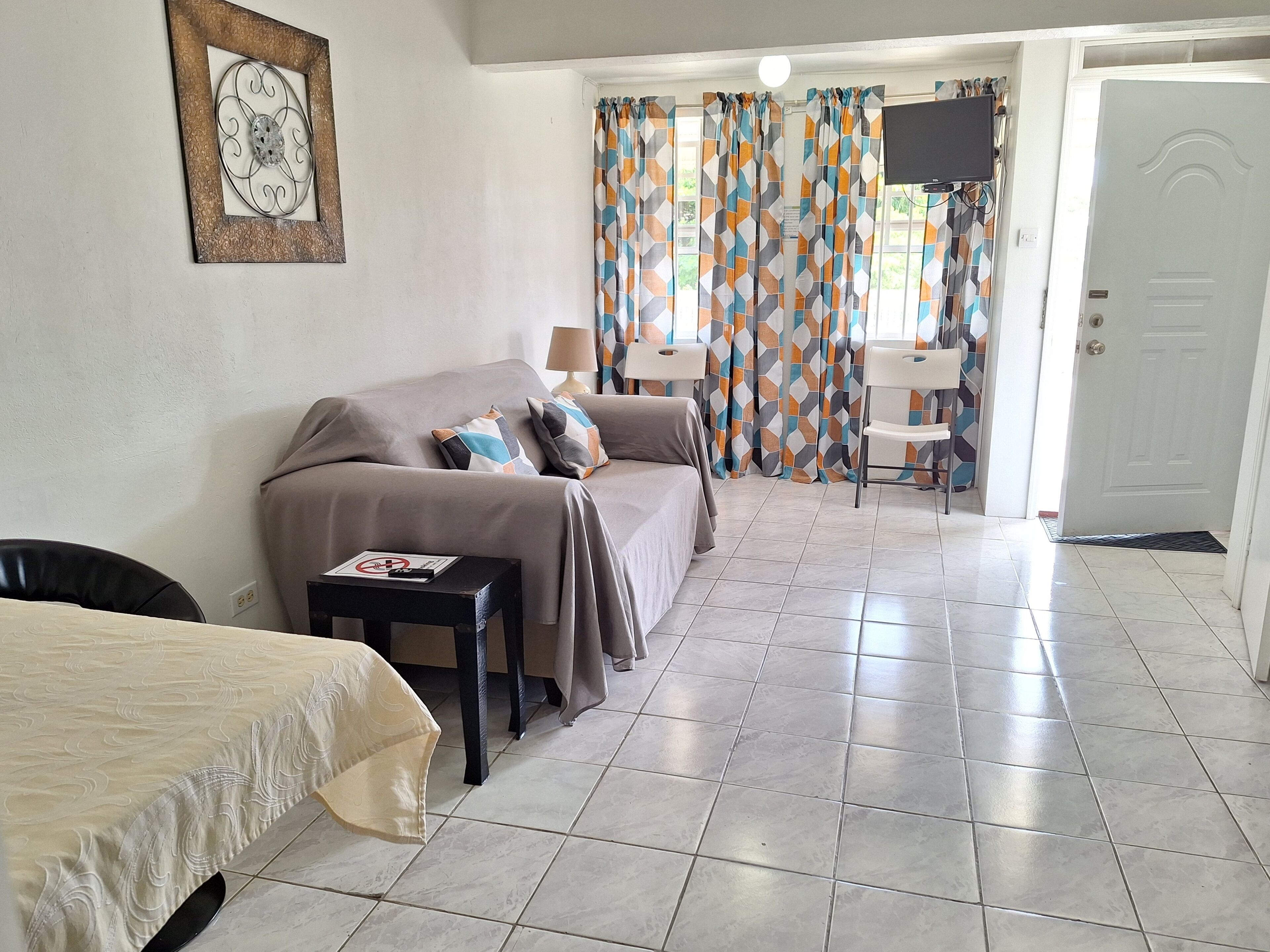 A hotel room with a bed, a small table, a chair, a TV, and a door.