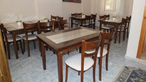 A dining area with multiple wooden tables and chairs, a calendar on the wall, and a window with curtains. - Arden Pansiyon (Çanakkale)