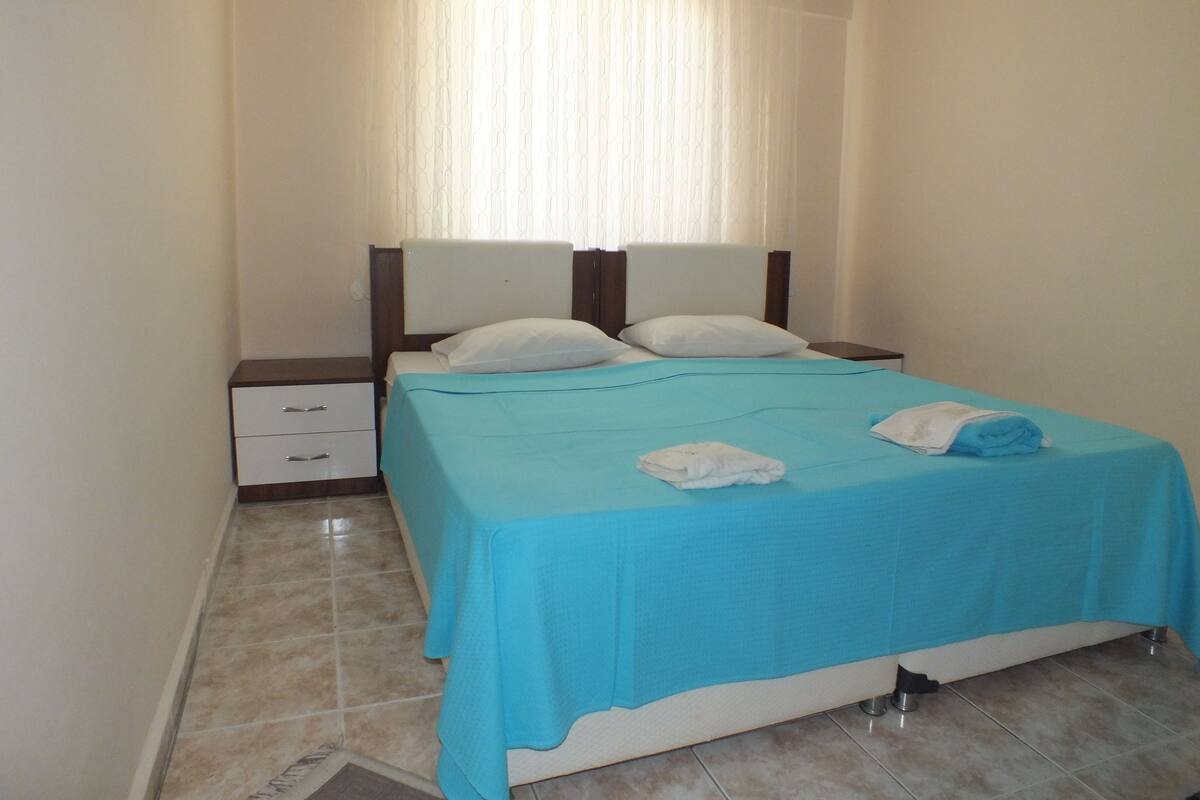 A neatly made bed with a blue bedspread, two pillows, and a folded towel on the side.