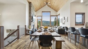 Ein geräumiger Essbereich mit hoher Decke, Steinwand und großen Fenstern mit Blick auf die Berge.