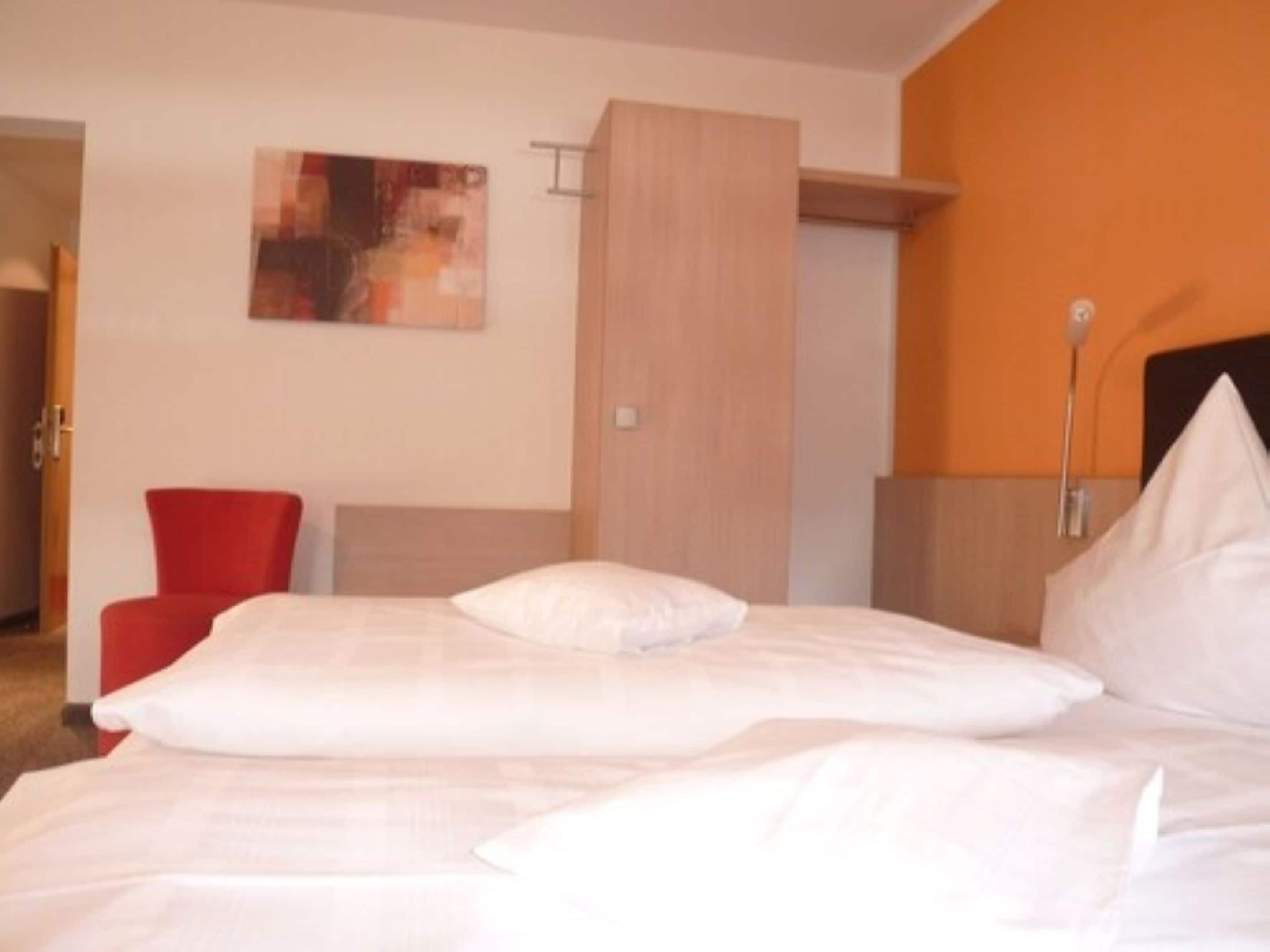 Una habitación de hotel con una cama grande, una silla roja y un cuadro en la pared.