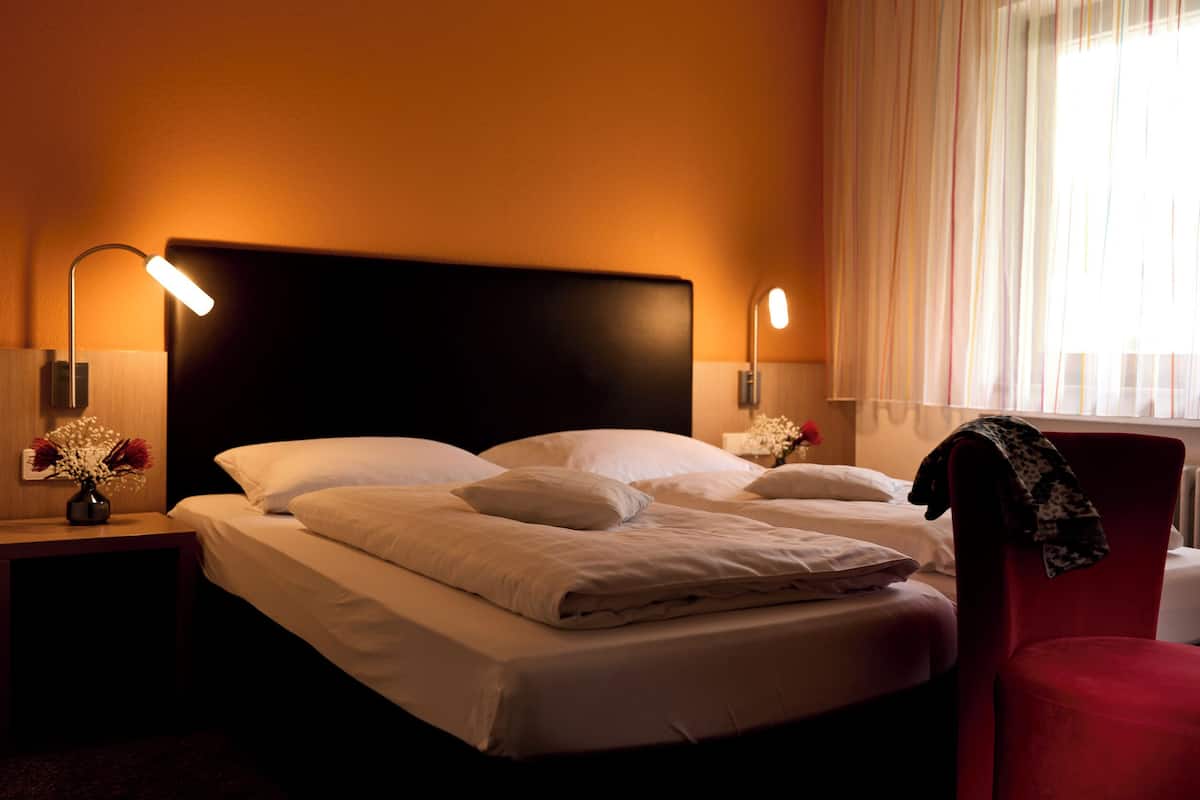 A neatly made bed with white linens, two bedside lamps, and a vase of flowers on a nightstand.
