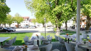 An outdoor dining area with tables and chairs, a view of parked cars, and trees in the background. - Hotel Gasthof Zum Bad (Langenau)