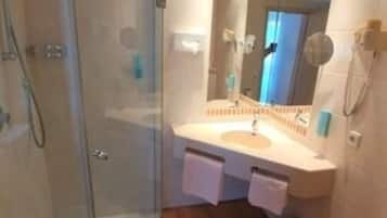 A bathroom with a glass shower enclosure, a white sink with a mirror, and a toilet.