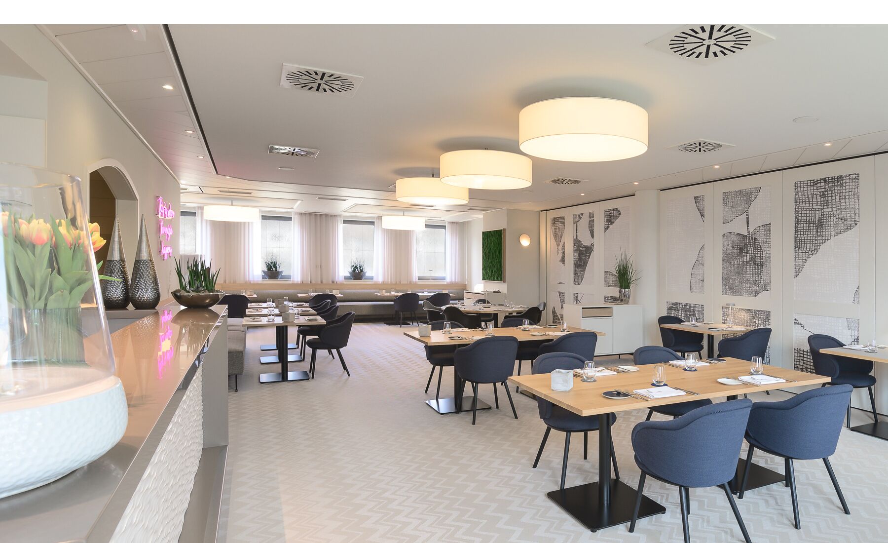 A modern dining area with multiple tables and chairs, large windows, and decorative wall art.