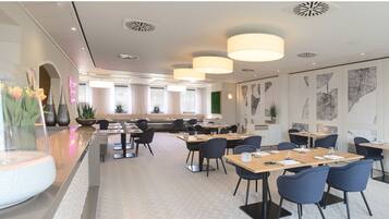 A modern dining area with multiple tables and chairs, large windows, and decorative wall art.