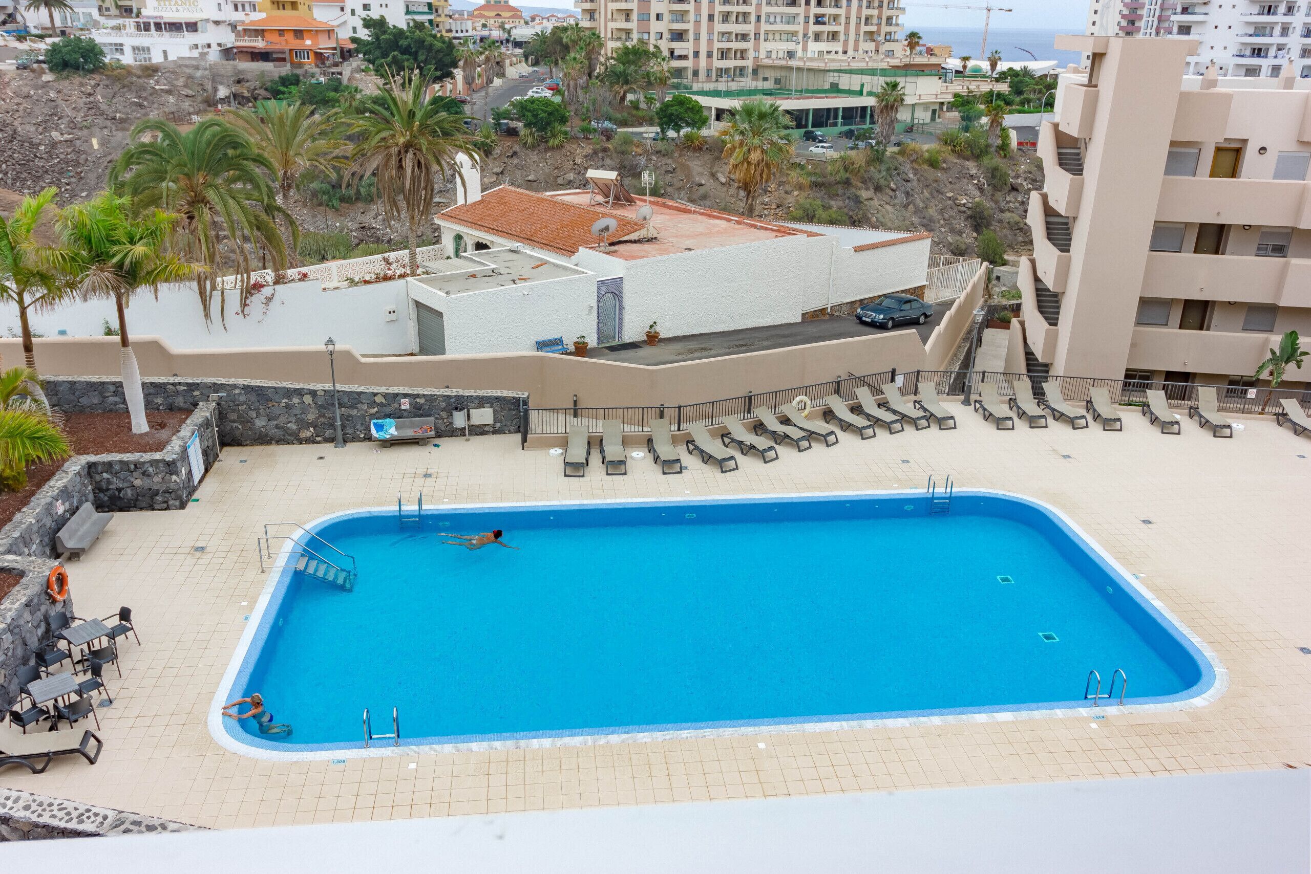 A rectangular swimming pool with a tiled deck, surrounded by lounge chairs and a lifeguard stand.