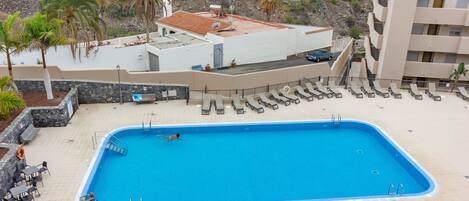 A rectangular swimming pool with a tiled deck, surrounded by lounge chairs and a lifeguard stand.