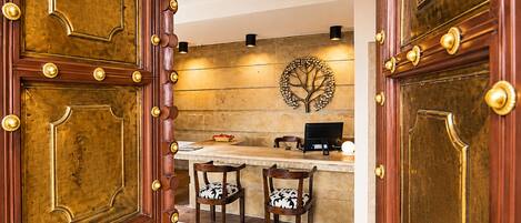 A reception area with a wooden desk, two chairs, a laptop, and a decorative wall piece.