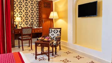 A hotel room with a bed, two chairs, a desk, a television, and patterned wallpaper.