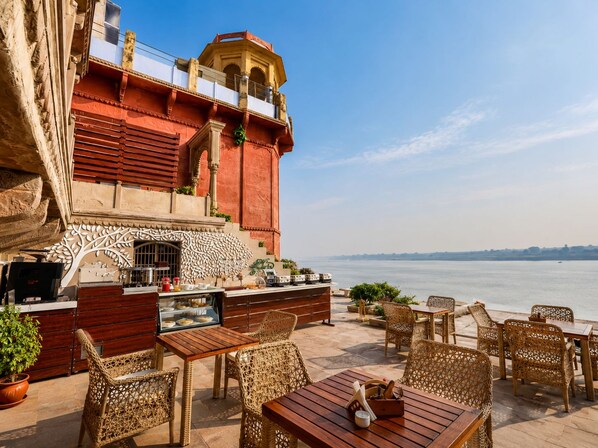 An outdoor seating area with wicker furniture and a view of the water. - Guleria Kothi (Varanasi)