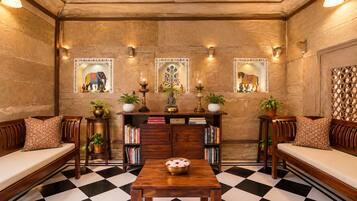 A room with a checkered floor, wooden furniture, a bookshelf, decorative wall art, and wall-mounted lighting.