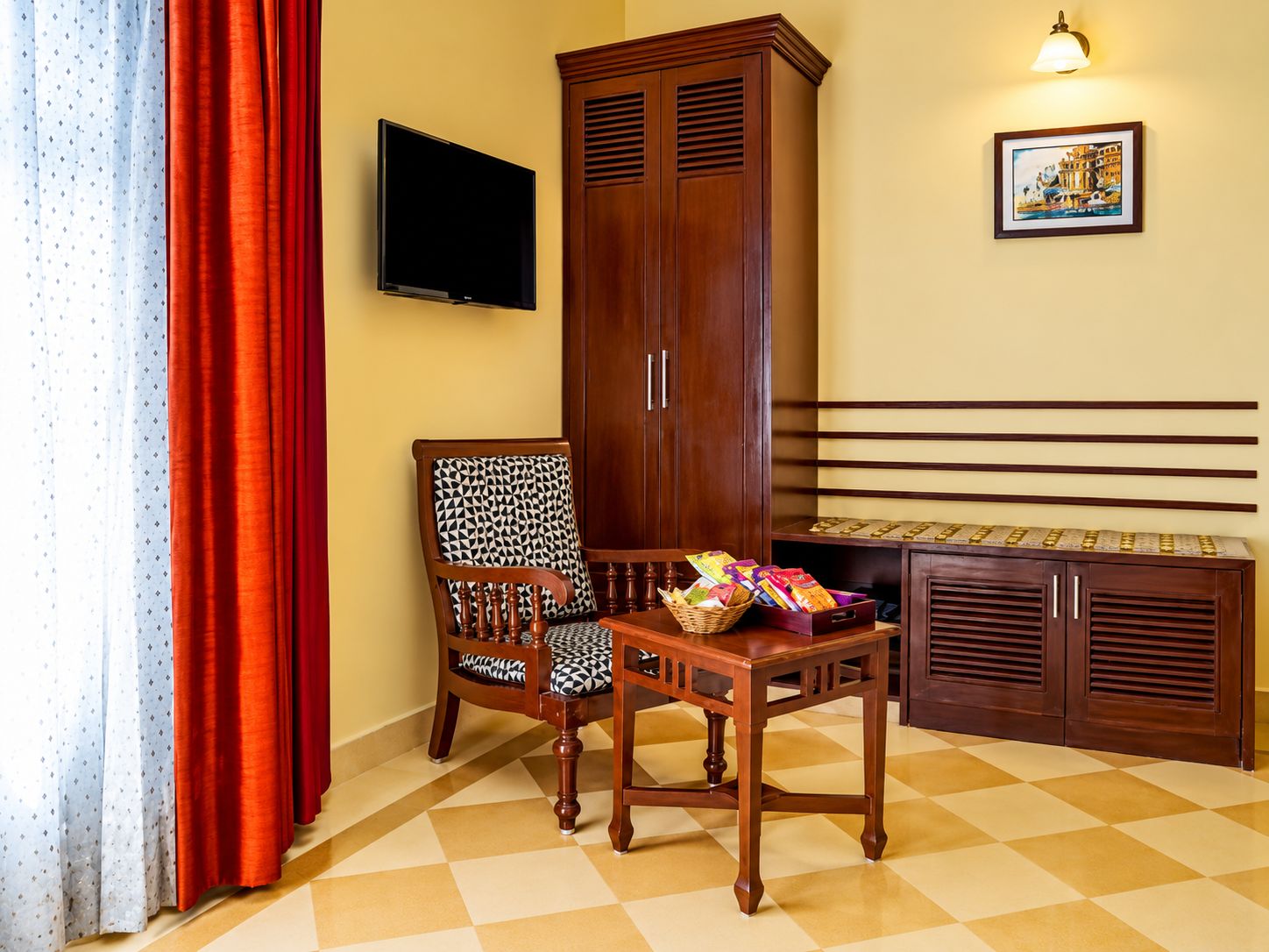 A room with a checkered floor, a wooden cabinet, a television mounted on the wall, and a chair with a patterned cushion.