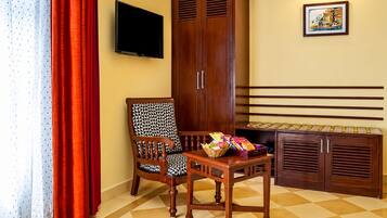 A room with a checkered floor, a wooden cabinet, a television mounted on the wall, and a chair with a patterned cushion.