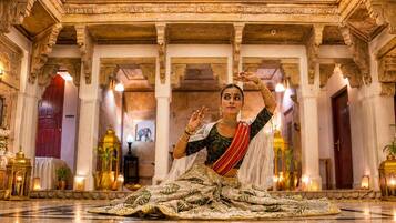 Una persona vestida con traje tradicional sentada en el suelo, en un interior espacioso y ricamente decorado con columnas y candelabros.