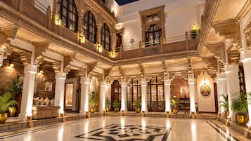 Un amplio patio con un diseño geométrico en el suelo, rodeado de columnas ornamentales y balcones, y decorado con plantas en macetas.