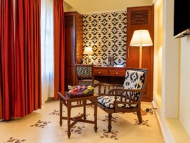 A hotel room with a desk, two chairs, a lamp, and a television.