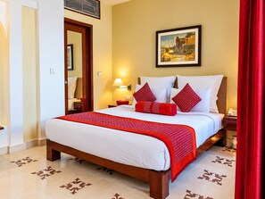 A hotel room with a large bed, a painting on the wall, and a red curtain. - Guleria Kothi (Varanasi)