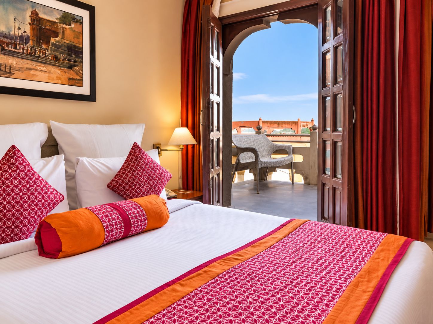 Una camera d'hotel con un letto grande, un quadro appeso al muro e un balcone aperto con vista su un edificio.