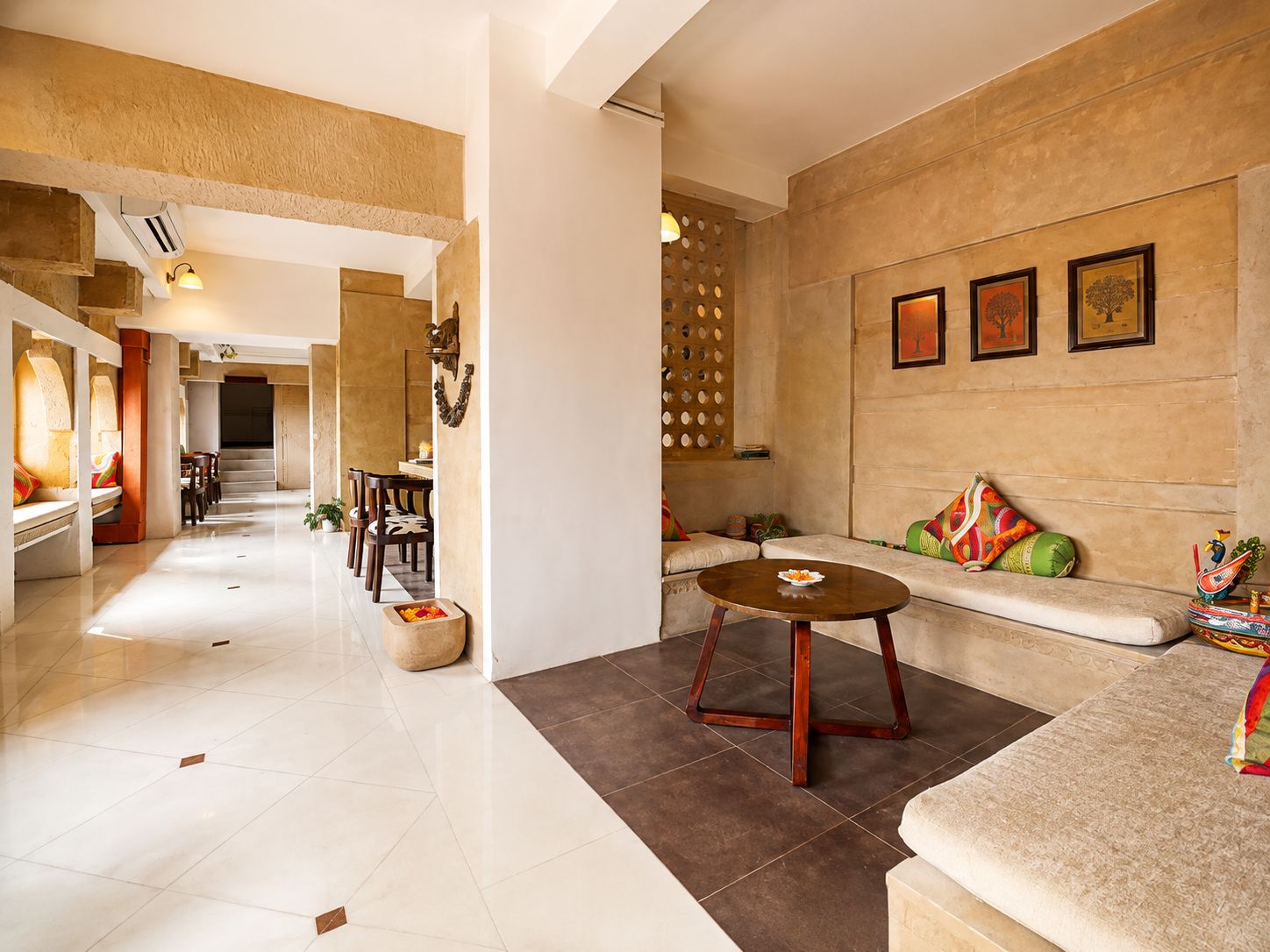 A spacious hotel lobby with a dining area, a seating area with a sofa and a coffee table, and a decorative wall with framed artwork.
