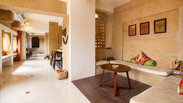 A spacious hotel lobby with a dining area, a seating area with a sofa and a coffee table, and a decorative wall with framed artwork.