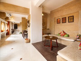 A spacious hotel lobby with a dining area, a seating area with a sofa and a coffee table, and a decorative wall with framed artwork.