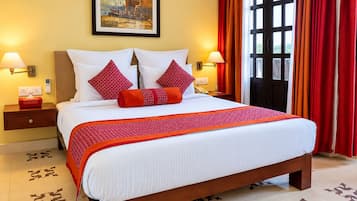 A hotel room with a large bed, two bedside tables, a painting on the wall, and a view through a window with curtains.