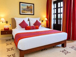 A hotel room with a large bed, two bedside tables, a painting on the wall, and a view through a window with curtains.